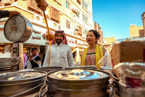 A female tourist in traditional dress standing at a local food stall in Saudi Arabia.
